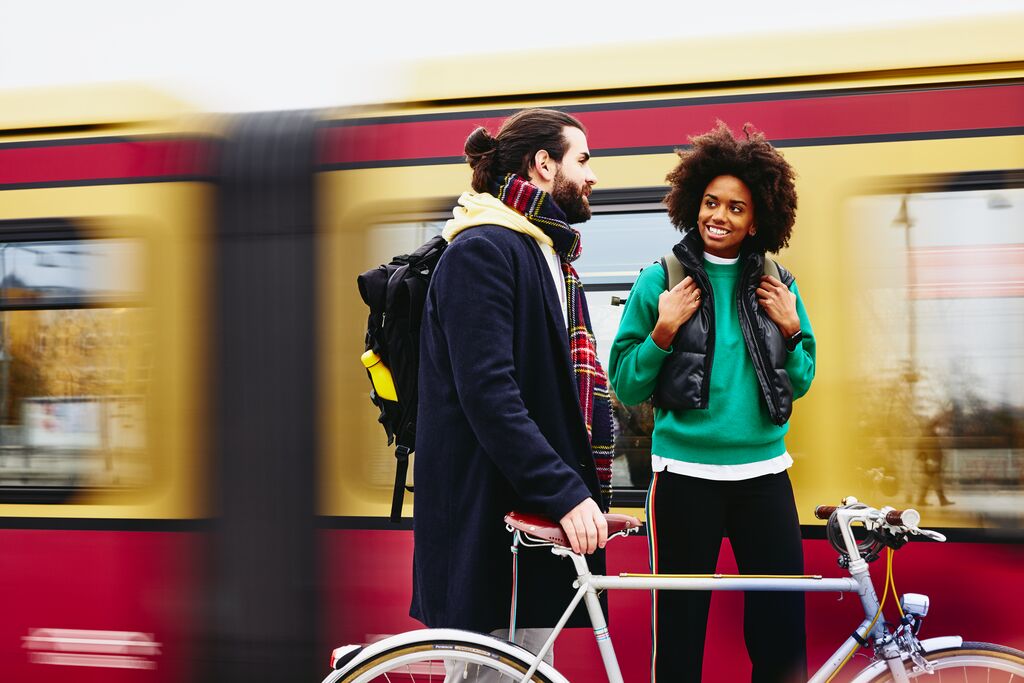 Man and woman standing on a train platform with a bike. Train in the background.
