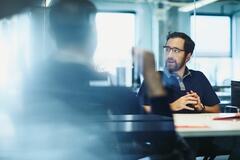 Man in a meeting, smiling looking away. Sitting down.