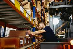 Man in elevator between  distribution center racks, picking up a box from a shelf
