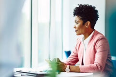 Kvinna sitter vid ett skrivbord och tittar ut genom fönstret