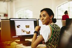 Woman sitting at her desk, looking away from computer screens displaying marketing content.