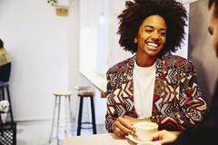 Smiling woman sitting at a table with coffee, smiling at someone.