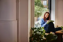 Female sitting in a window seat working on a tablet with a touch pen