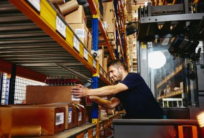 Man in elevator between  distribution center racks, picking up a box from a shelf