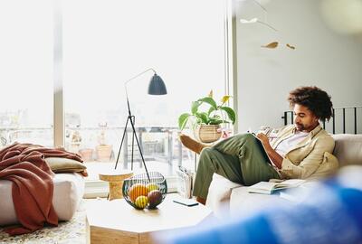 en man sitter i soffan hemma, skriver i ett anteckningsblock, fokuserat