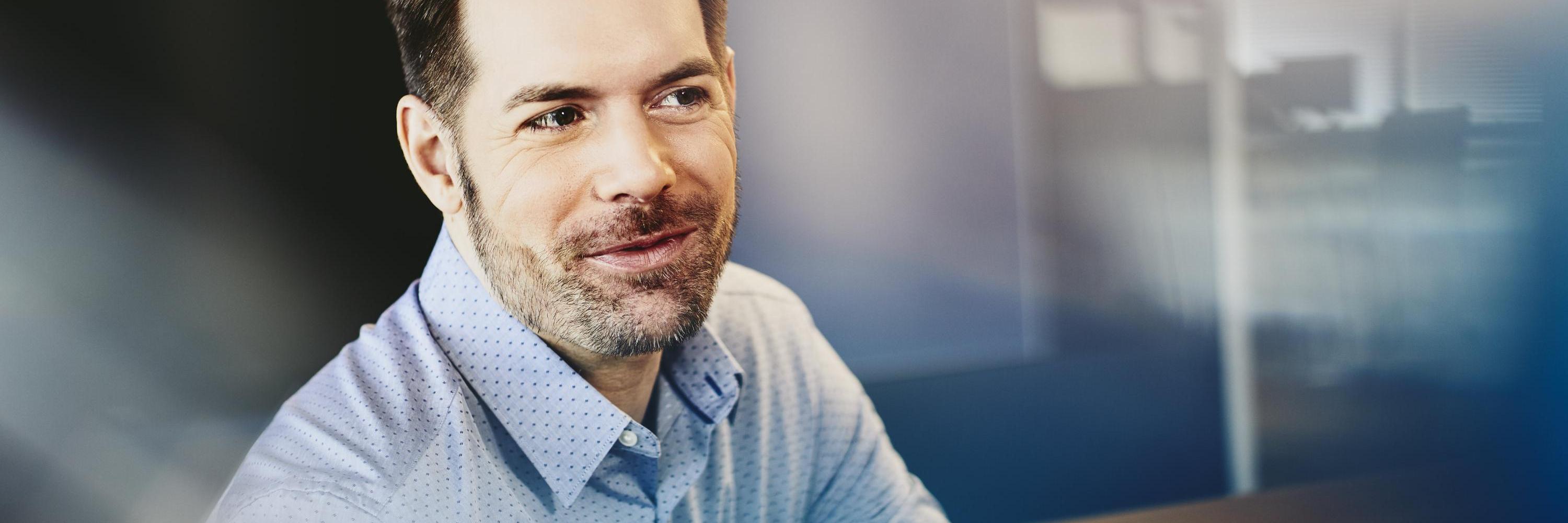Man in a shirt in an office. Primary color: blue.