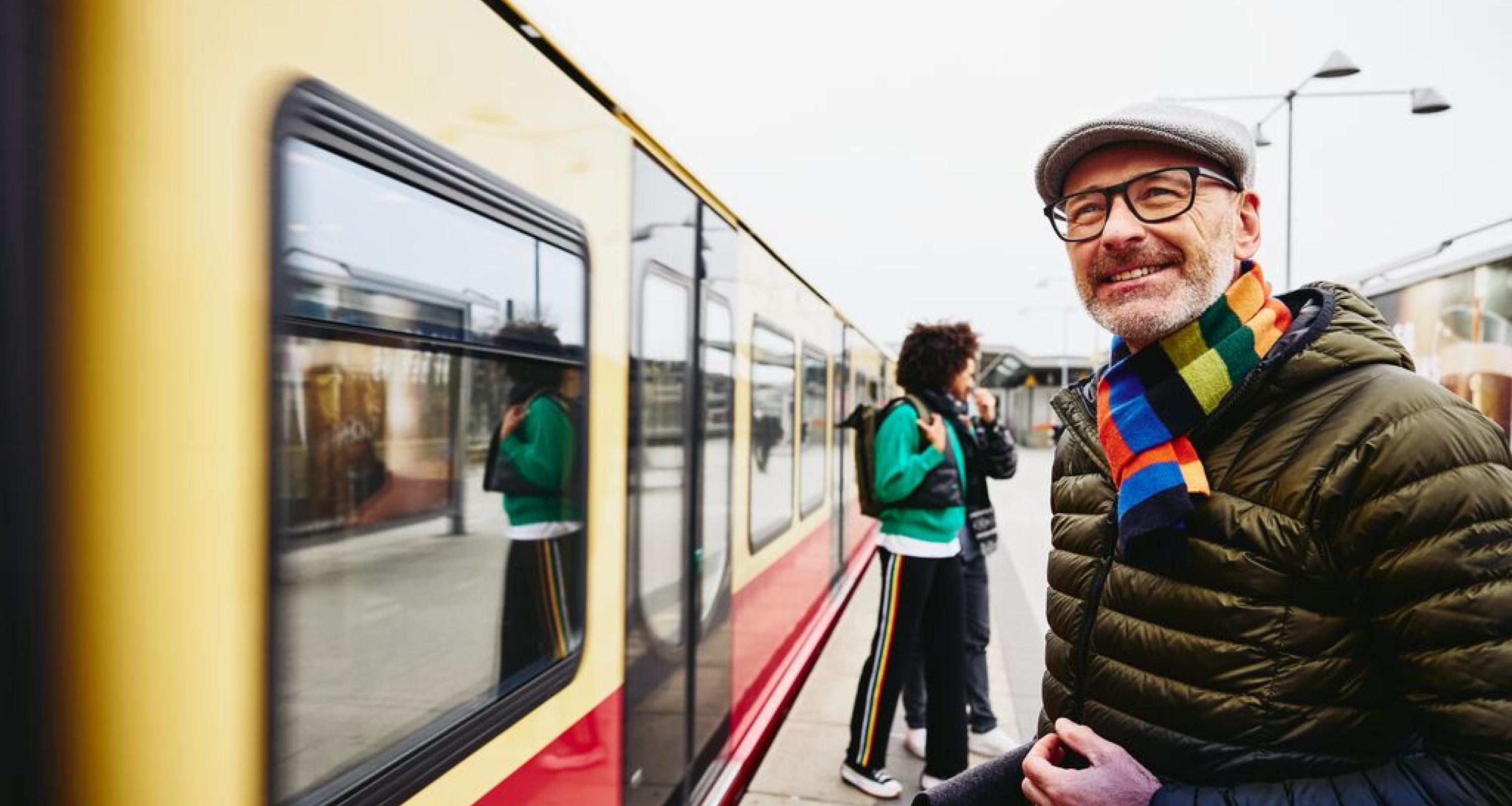 Man standing next to a train. Two people getting out of a train in the background