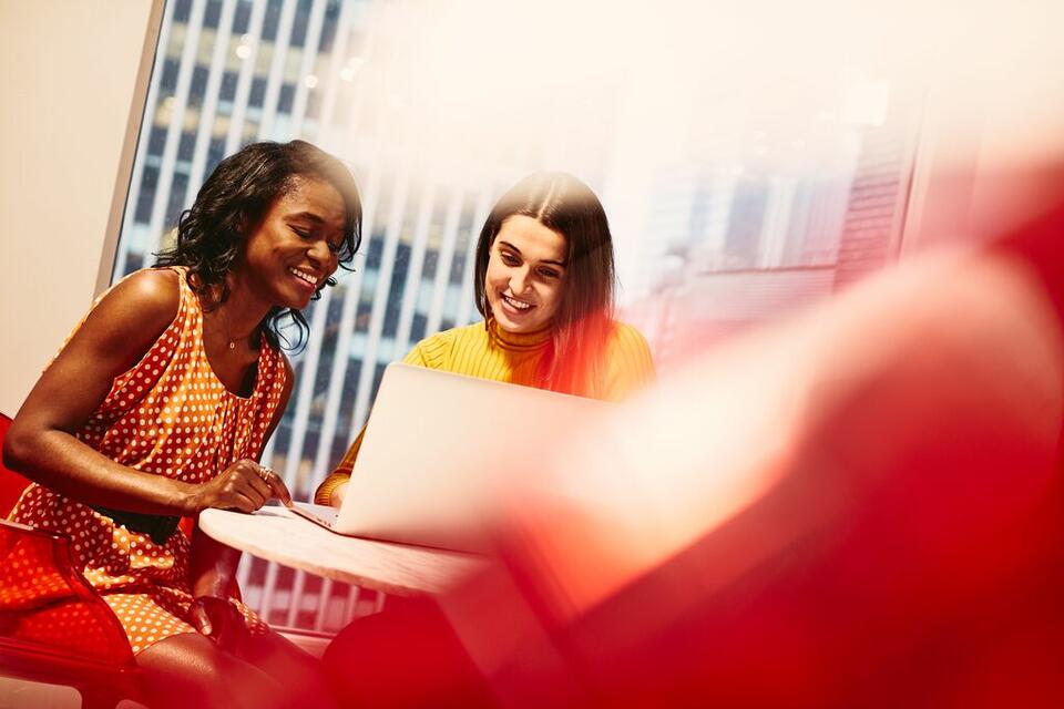 two woman working behind laptop