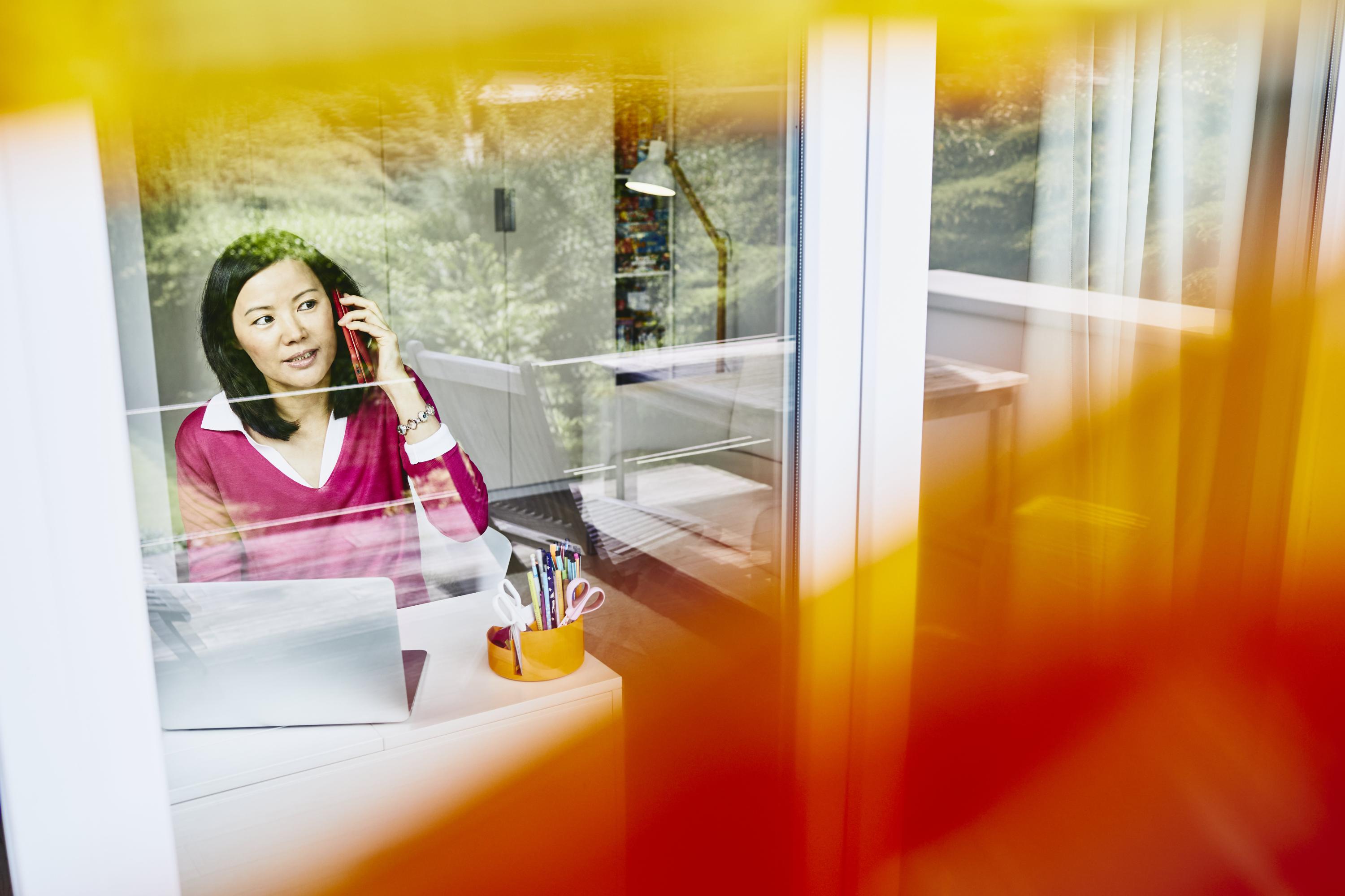 en kvinna syns innanför en glasruta, pratar i telefon och tittar samtidigt ut genom fönstret