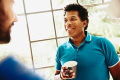 smiling man holding a coffee cup having a chat with someone