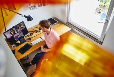 en man sitter vid sitt hemmakontor, sett ovanifrån, pratar med sina kollegor i ett onlinemöte