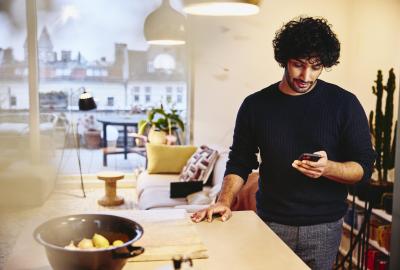 en man står vid sidan av sin köksö, hemma, tittar på telefonen