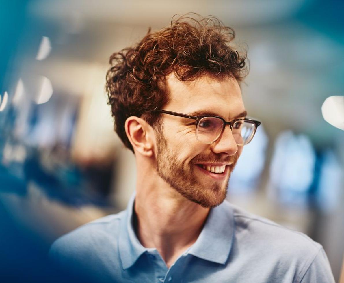 candidate in focus, smiling man in the office with glasses and blue shirt