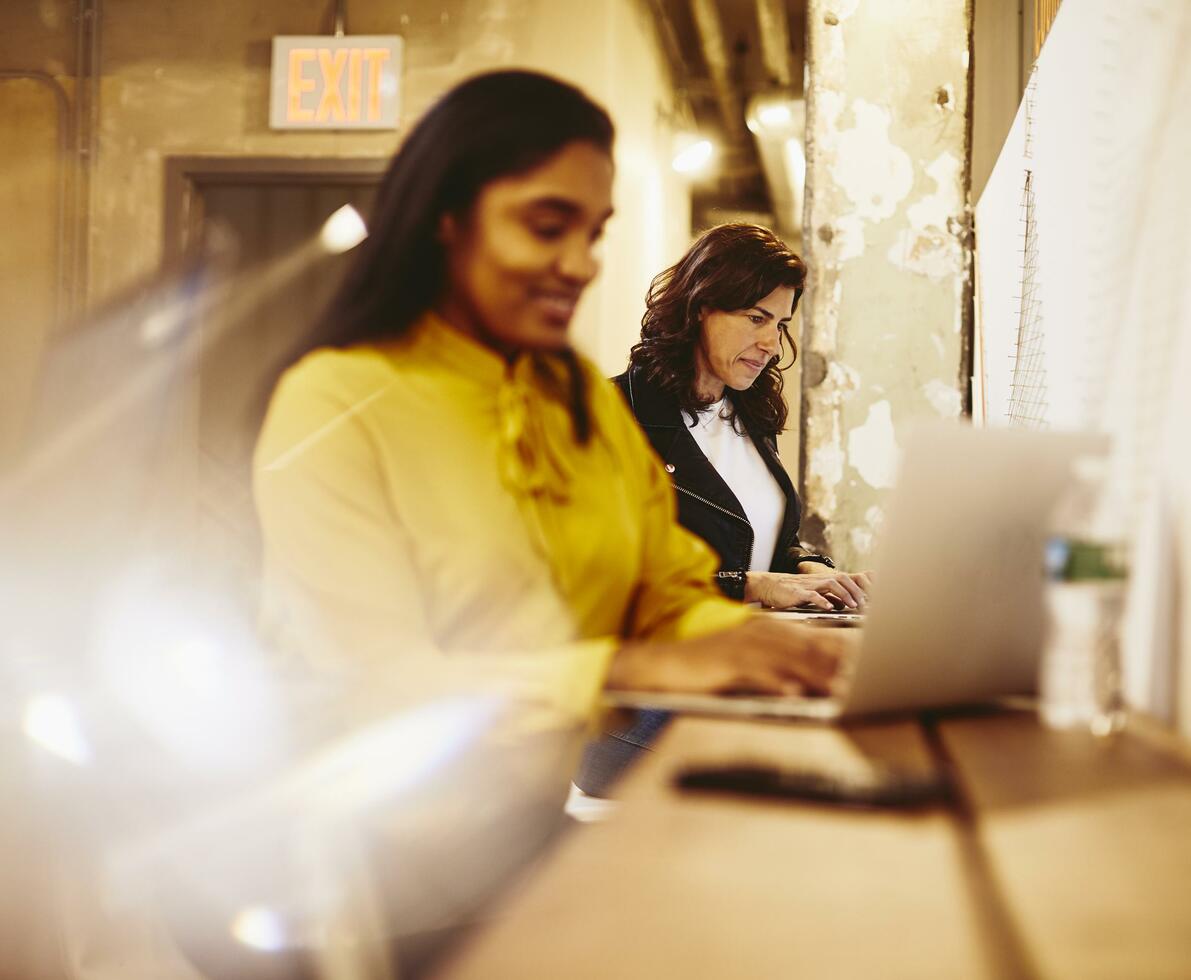 två kvinnor arbeta på sina laptops, bredvid varandra på kontoret