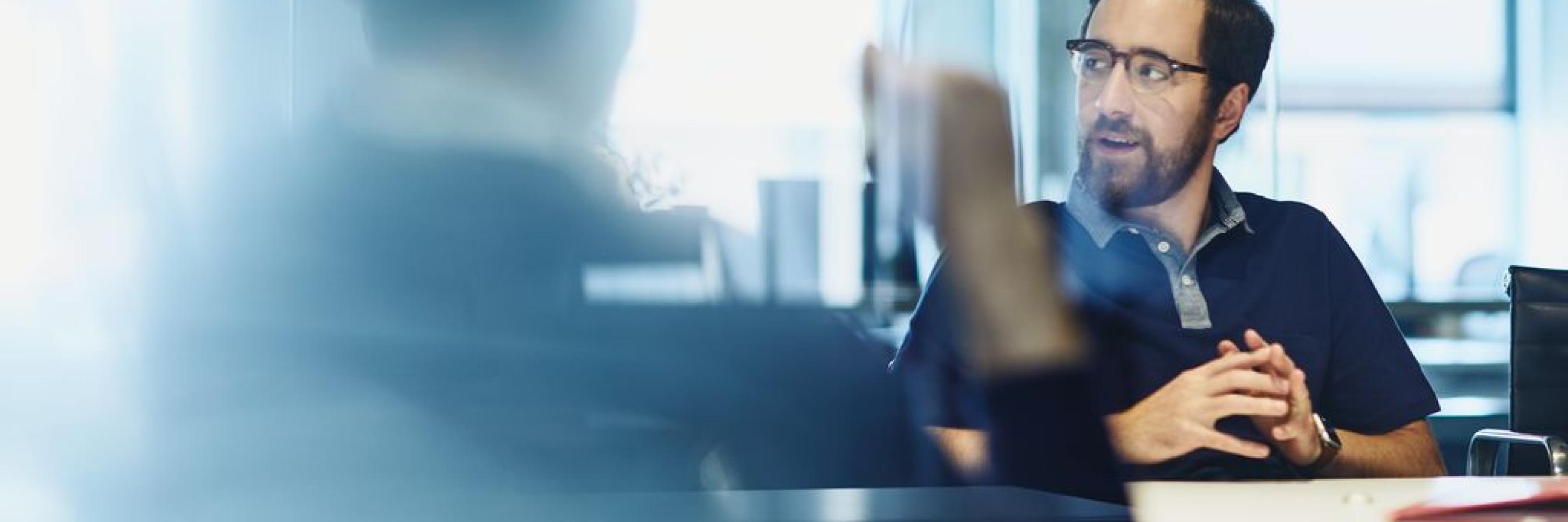 Man in a meeting, smiling looking away. Sitting down.