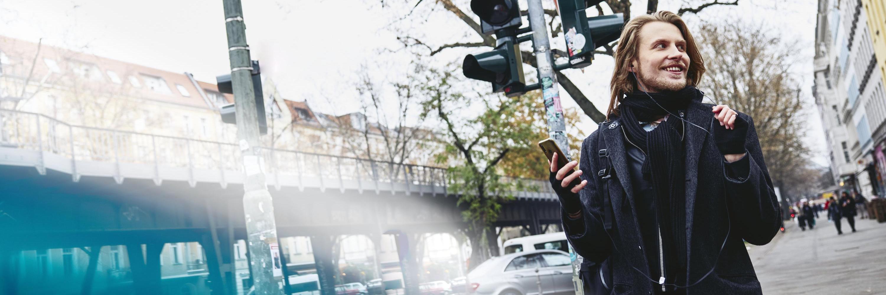 Man walking outside holding his phone with earphones in.