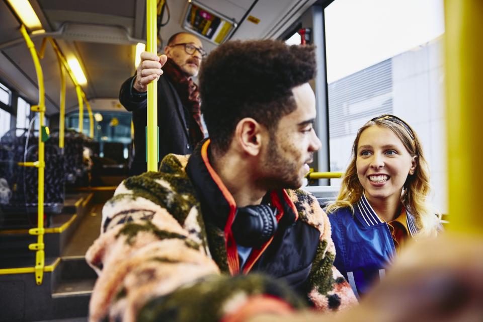 en kvinna och man har en konversation på bussen. Andra personer i bakgrunden